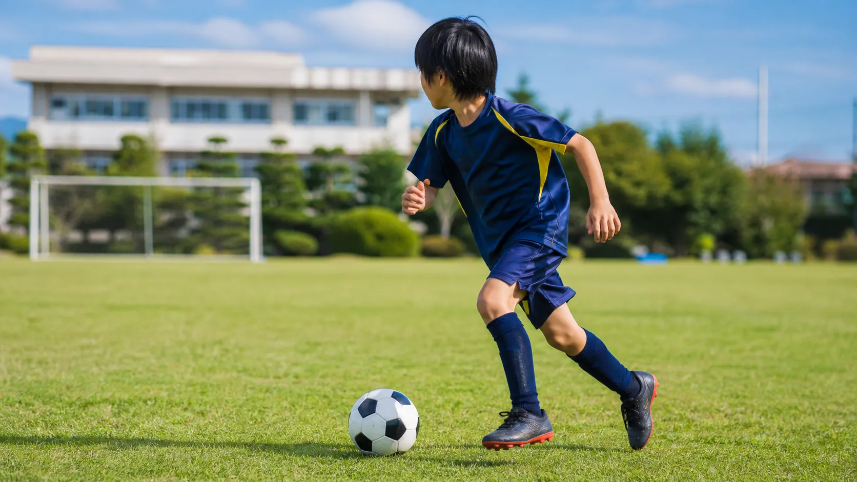 芝生でサッカーボールを追う日本人の子ども