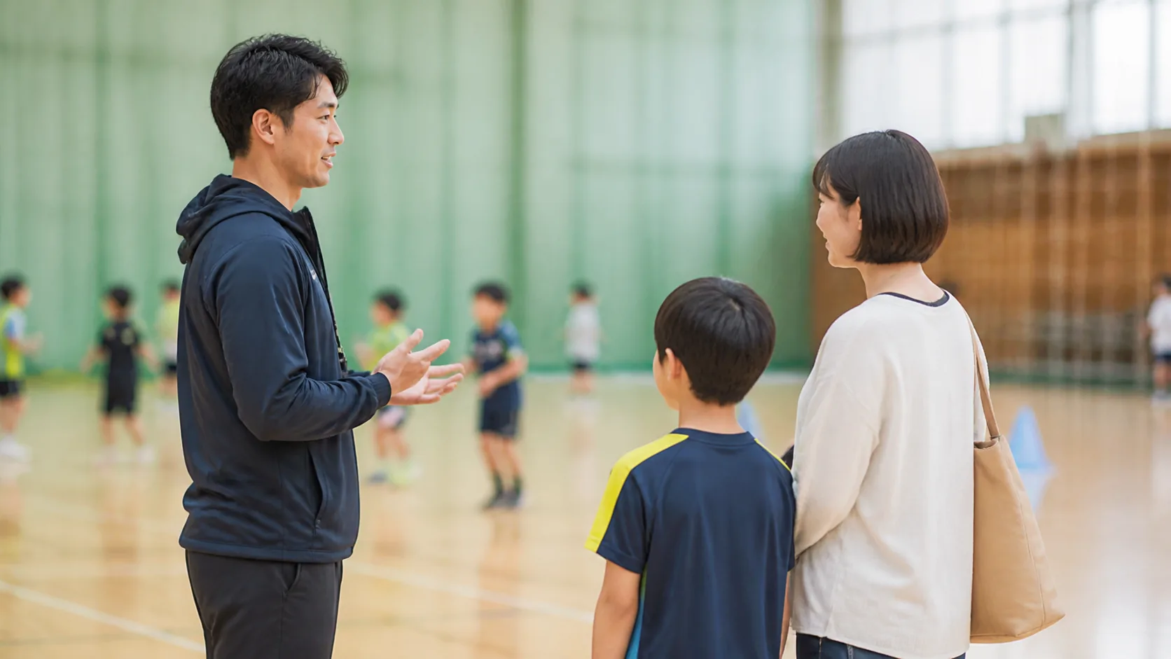 教室の見学中に指導者へ相談する日本人の親子